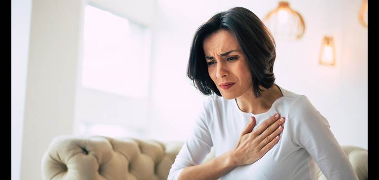 A woman holds her hand to her chest while experiencing discomfort