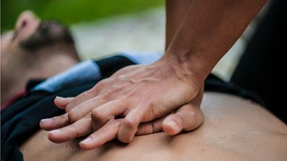 A man lies flat while someone does CPR on his bare chest