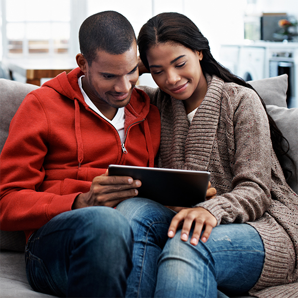 Couple sitting on a sofa holding a tablet device