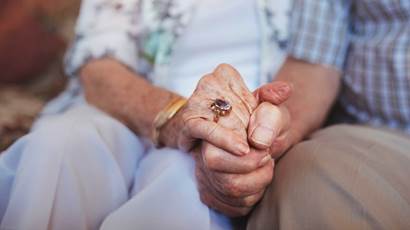 Cropped shot of elderly couple holding hands while sitting together at home