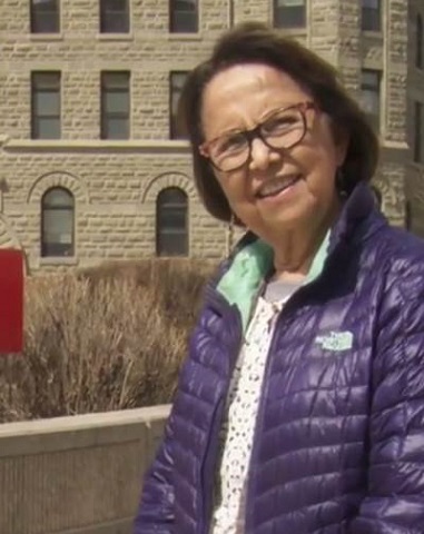 Esther Sanderson wears a purple jacket and smiles beside a University of Winnipeg sign.