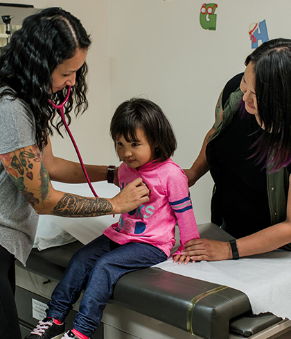 A doctor performs a check-up on a child with a stethoscope while her mother holds the child’s hand.