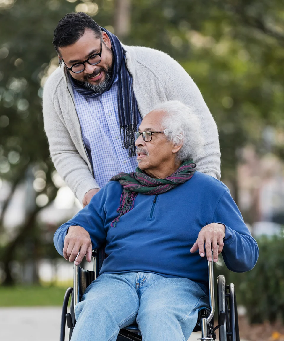 A senior man on a wheelchair talking with his caregiver.