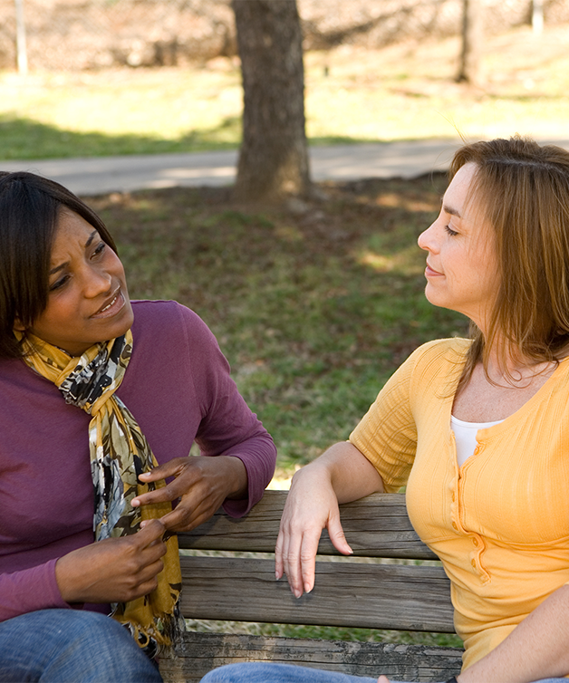Two women having a conversation while sitting on a bench outdoors.