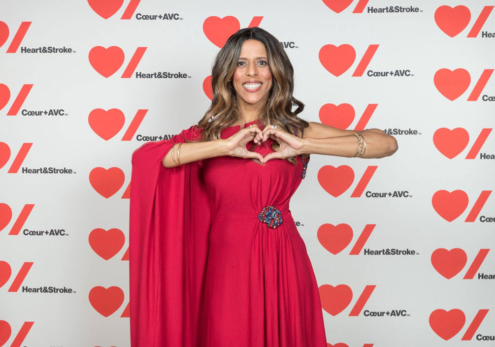 Caroline Lavallée wears a red gown and holds her hands in a heart shape.