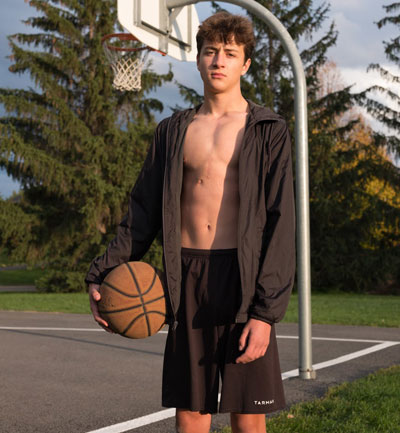 Olivier Lanthier stands in front of an outdoor basketball net holding a basketball